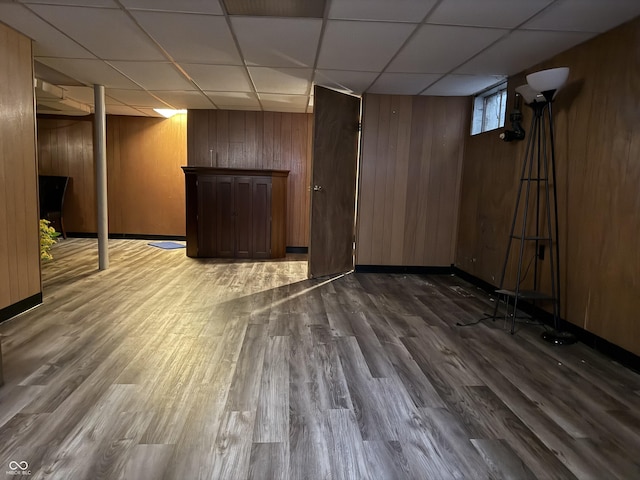 basement with wooden walls, baseboards, wood finished floors, and a drop ceiling