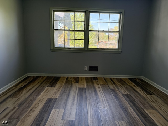 empty room featuring visible vents, baseboards, and dark wood-style flooring