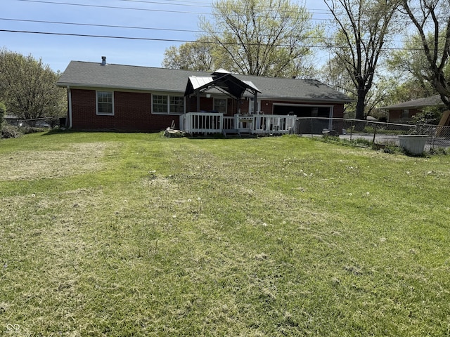 rear view of property with fence, a wooden deck, brick siding, and a yard