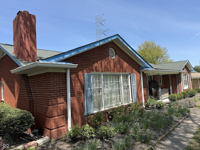 view of side of home with a chimney, brick siding, and roof with shingles