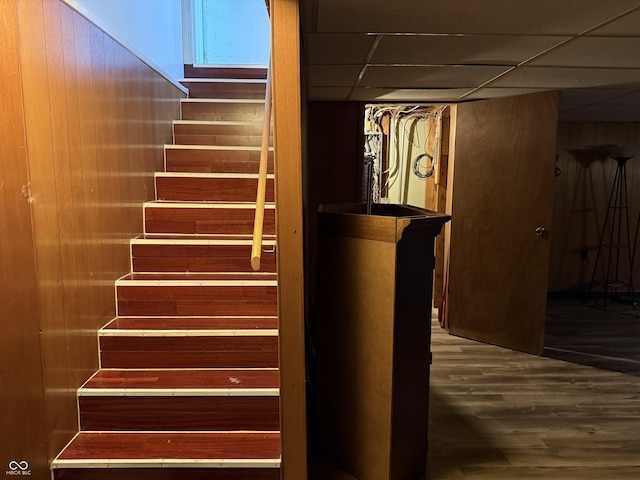 staircase featuring wood finished floors, wood walls, and a drop ceiling