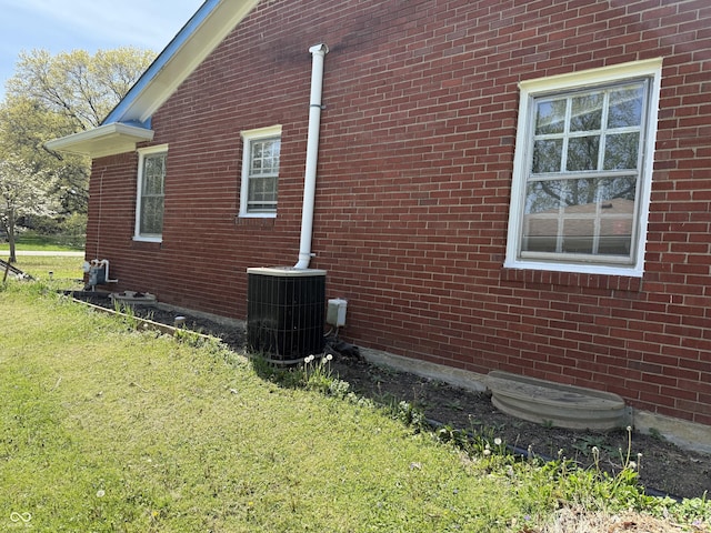 view of side of home featuring cooling unit, a yard, and brick siding
