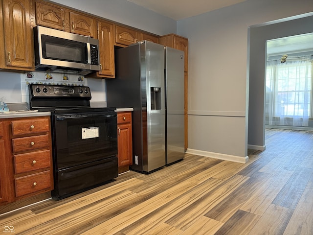 kitchen featuring brown cabinetry, baseboards, appliances with stainless steel finishes, and light wood-type flooring