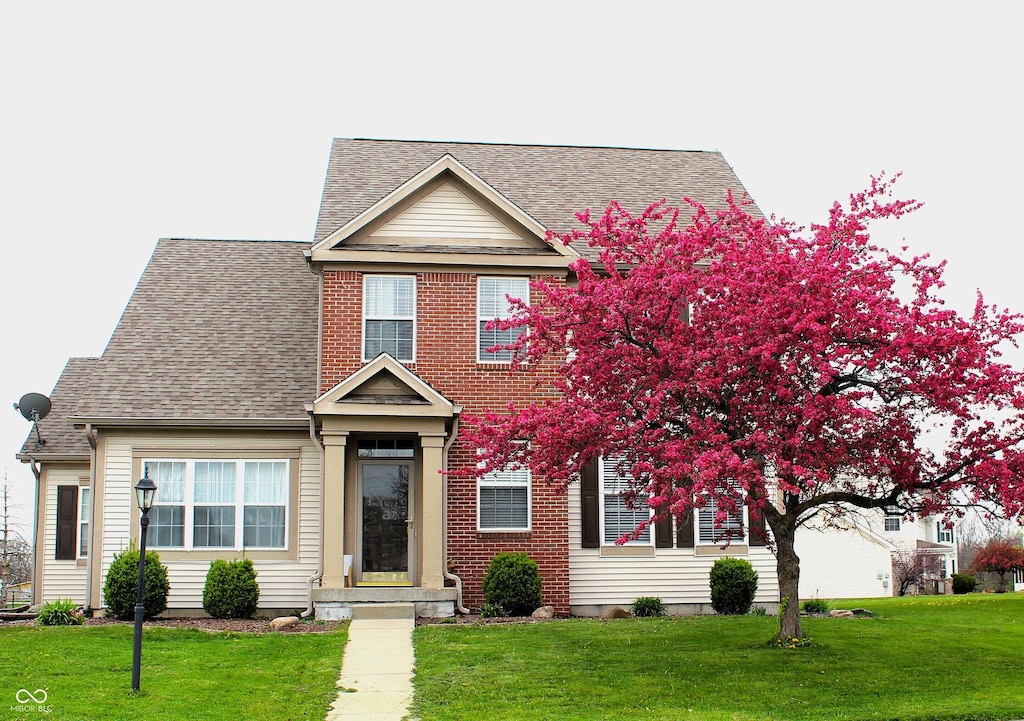view of front facade with a front lawn, brick siding, and roof with shingles