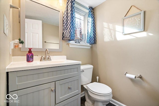 bathroom with toilet, baseboards, and vanity