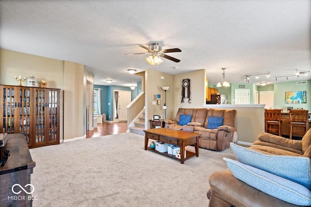 living area featuring carpet flooring, a textured ceiling, ceiling fan, and stairway