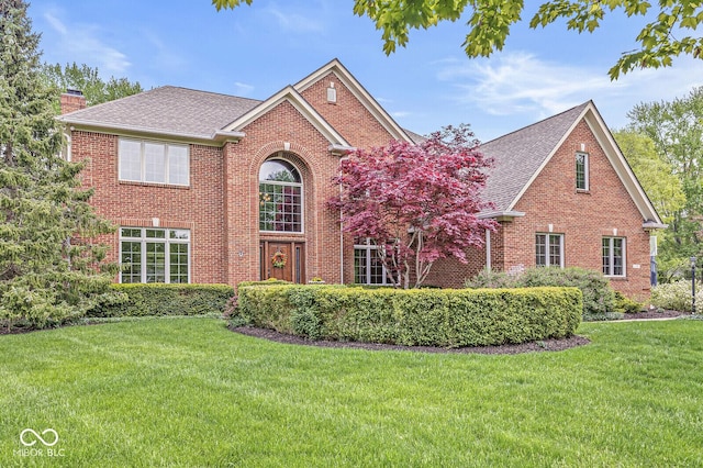 view of front of house featuring brick siding, a chimney, a shingled roof, and a front lawn
