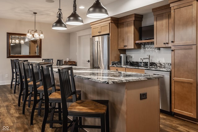 kitchen featuring dark stone countertops, stainless steel appliances, a kitchen bar, a sink, and dark wood-style floors