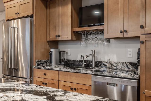 kitchen with a sink, brown cabinets, dark stone countertops, and appliances with stainless steel finishes