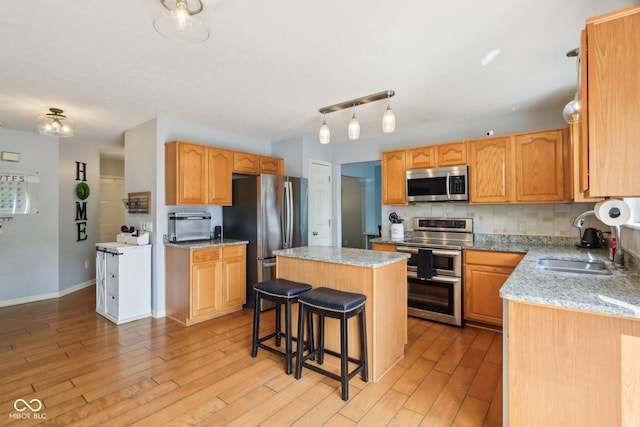 kitchen featuring appliances with stainless steel finishes, a sink, light wood-type flooring, a center island, and a kitchen bar