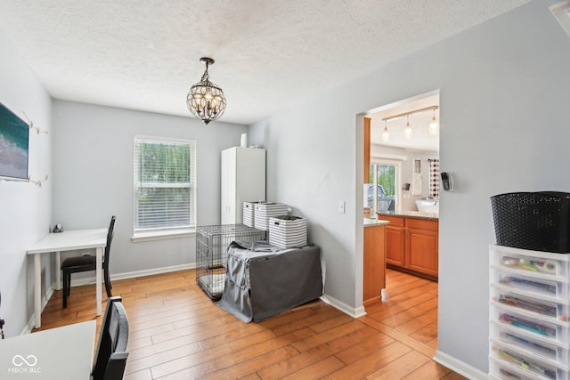 dining area featuring light wood finished floors, a chandelier, a textured ceiling, and baseboards