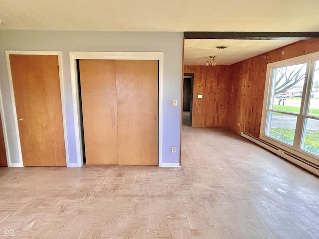 unfurnished bedroom with baseboard heating, baseboards, wooden walls, and a closet