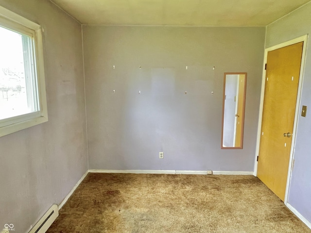carpeted spare room featuring a baseboard heating unit and baseboards
