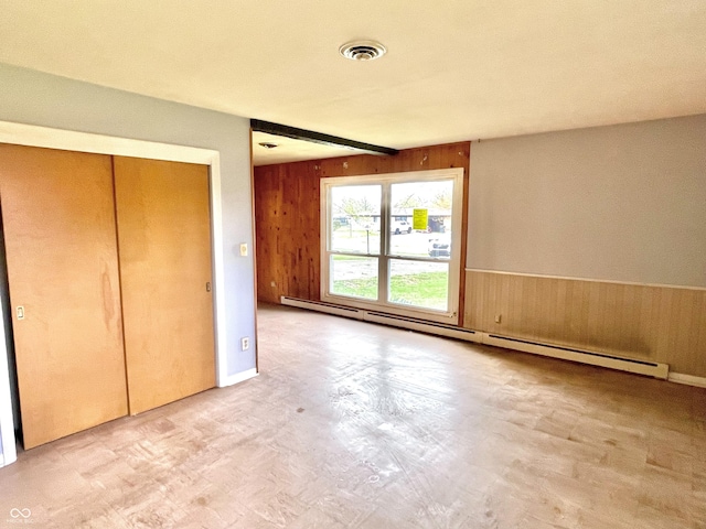 unfurnished bedroom featuring a wainscoted wall, wooden walls, visible vents, a closet, and a baseboard radiator