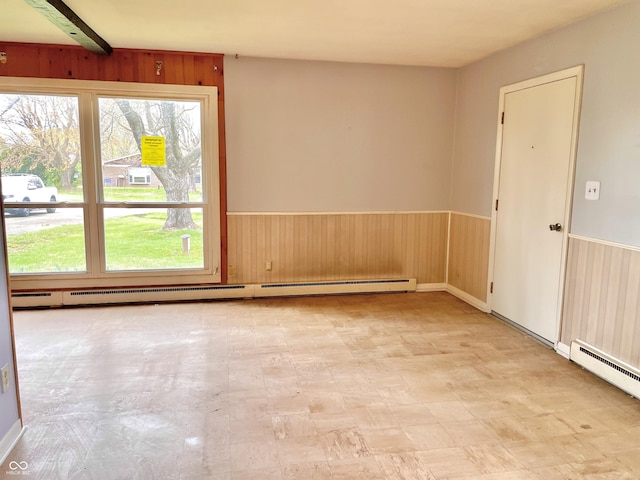 spare room with a baseboard heating unit, a wainscoted wall, wood walls, and light floors