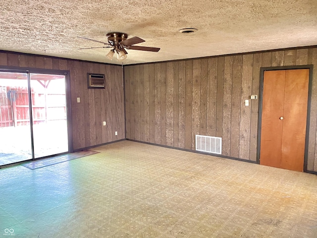 unfurnished room with wooden walls, visible vents, tile patterned floors, and a ceiling fan