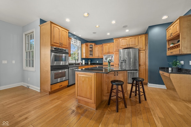 kitchen with a kitchen breakfast bar, stainless steel appliances, light wood-type flooring, and a sink