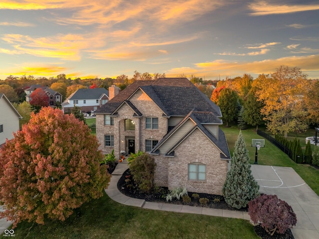 french country home with a chimney, a front lawn, a shingled roof, fence, and brick siding