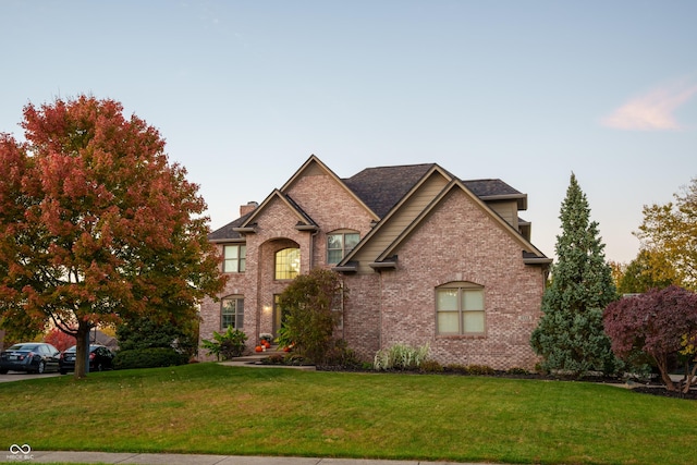 french country style house featuring brick siding, a chimney, and a front yard