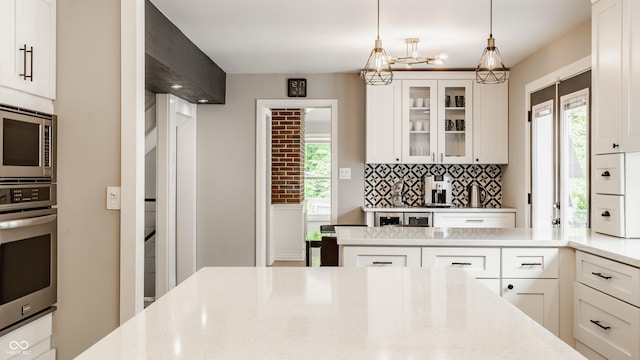 654 E 79th St, Indianapolis, IN 46240 - kitchen with appliances with stainless steel finishes, light stone counters, a chandelier, glass insert cabinets, and tasteful backsplash