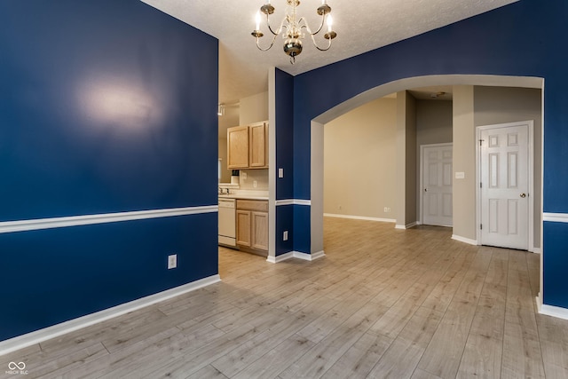 empty room with arched walkways, a chandelier, light wood-style floors, baseboards, and a textured ceiling