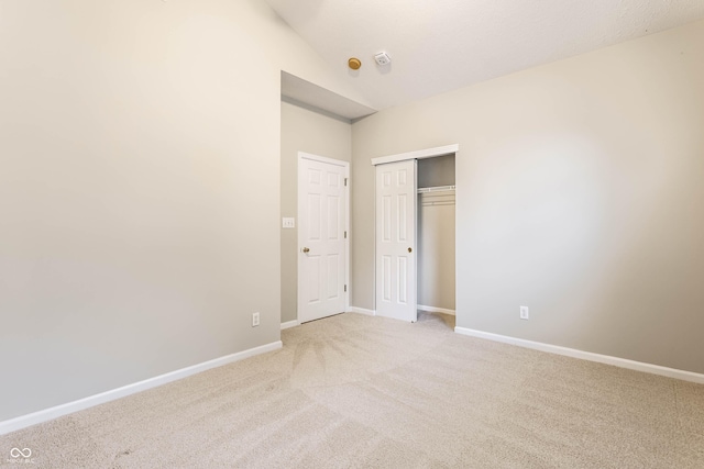 unfurnished bedroom with light colored carpet, baseboards, a closet, and vaulted ceiling