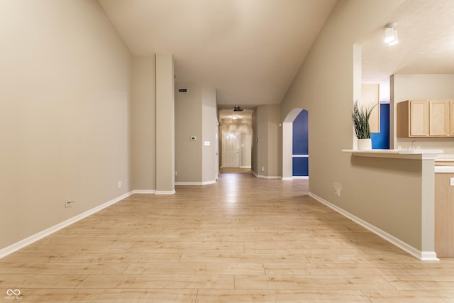 hallway with arched walkways, light wood finished floors, and baseboards