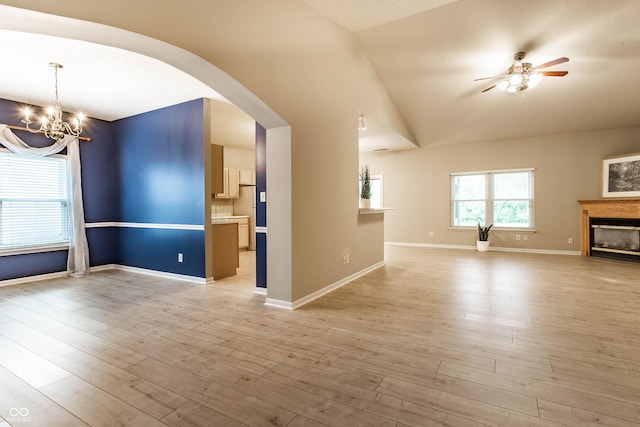 unfurnished living room with ceiling fan, arched walkways, lofted ceiling, a chandelier, and a glass covered fireplace