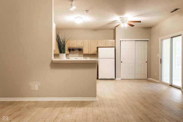kitchen with freestanding refrigerator, ceiling fan, light brown cabinets, light wood-style flooring, and a peninsula