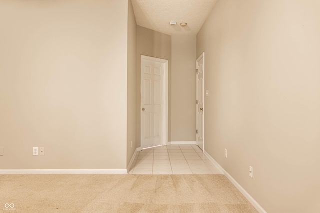 hallway with carpet floors, tile patterned flooring, baseboards, and a textured ceiling