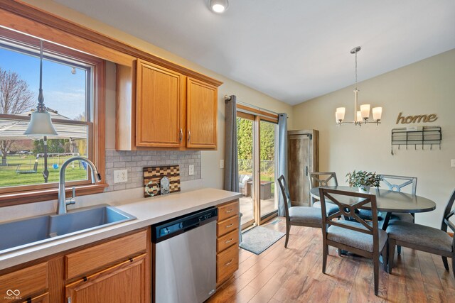 kitchen with light countertops, stainless steel dishwasher, a sink, light wood-style floors, and a notable chandelier