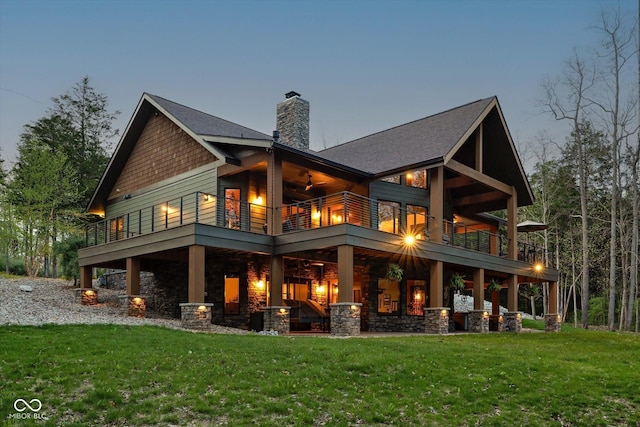 back of property with a balcony, a yard, a chimney, and stone siding