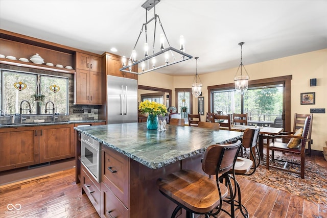 kitchen with built in appliances, a chandelier, hardwood / wood-style floors, and a breakfast bar area