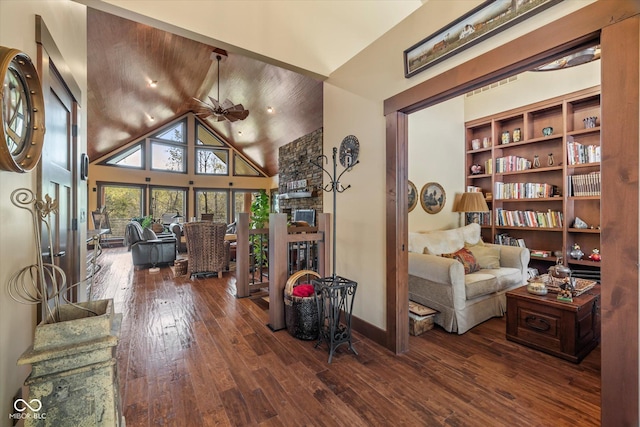 living area featuring a stone fireplace, hardwood / wood-style flooring, high vaulted ceiling, ceiling fan, and baseboards