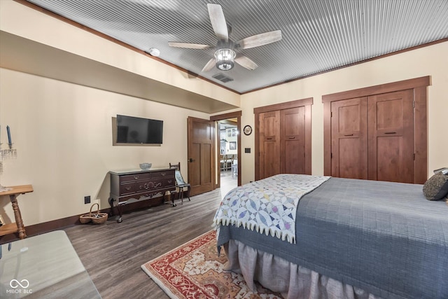 bedroom featuring dark wood-style flooring, two closets, baseboards, and a ceiling fan
