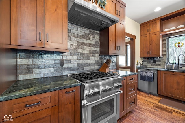 kitchen with stainless steel appliances, extractor fan, a sink, decorative backsplash, and brown cabinets