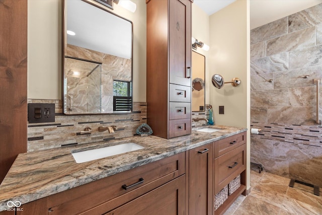 bathroom with tiled shower, double vanity, tasteful backsplash, and stone finish floors
