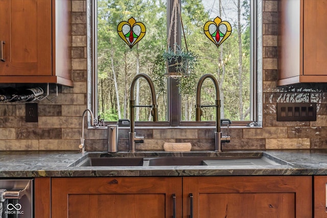 kitchen featuring brown cabinetry, backsplash, dark stone countertops, and a sink