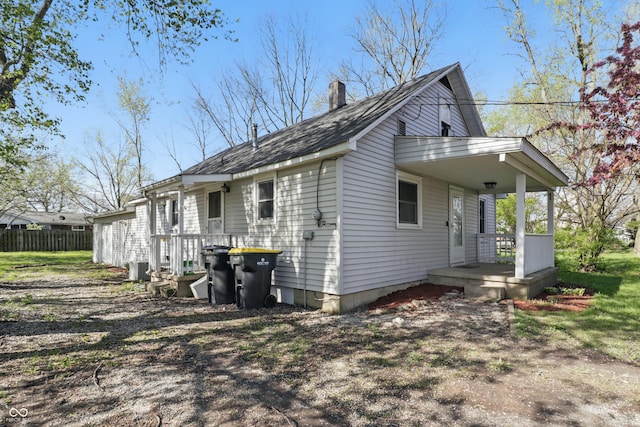 view of home's exterior with a chimney, fence, central AC, a porch, and roof with shingles