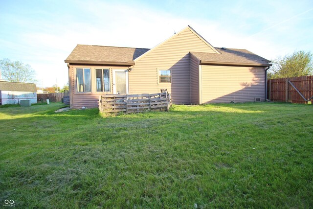 rear view of house with a fenced backyard, a shingled roof, and a lawn
