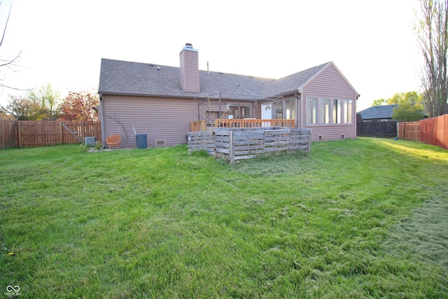 back of property with a chimney, a wooden deck, a yard, and a fenced backyard