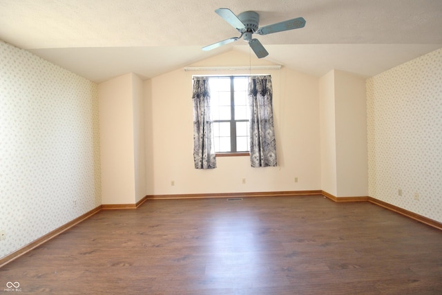 empty room with ceiling fan, lofted ceiling, wood finished floors, and wallpapered walls