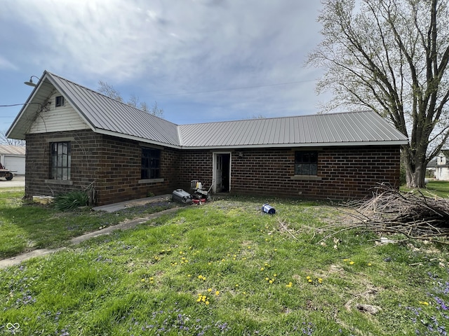 back of house featuring brick siding, metal roof, and a lawn