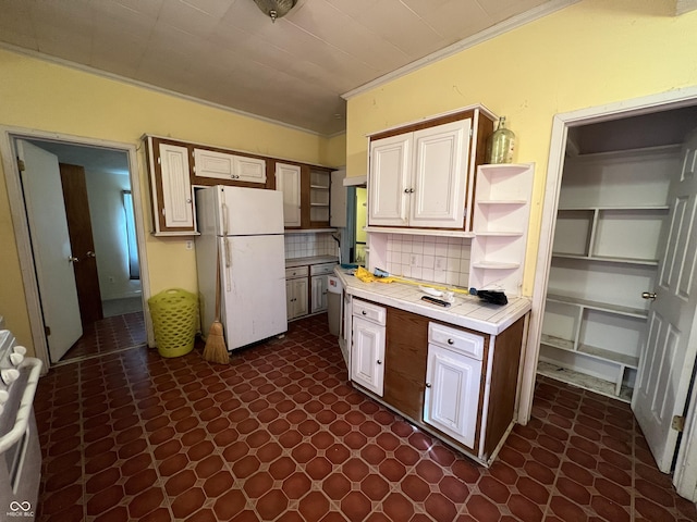 kitchen featuring open shelves, tile counters, freestanding refrigerator, ornamental molding, and backsplash
