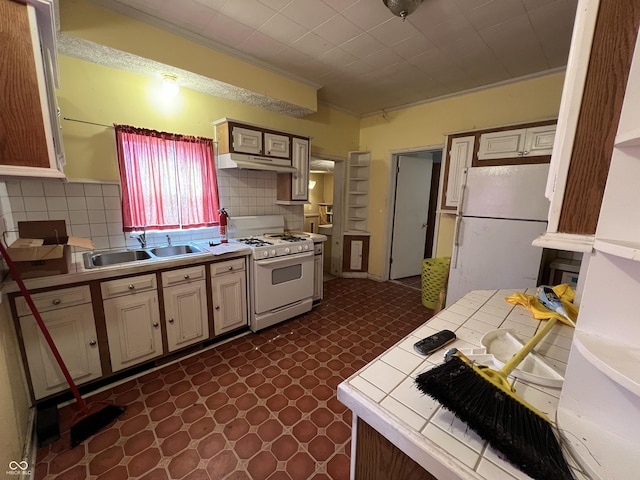 kitchen featuring a sink, tile counters, under cabinet range hood, dark floors, and white appliances