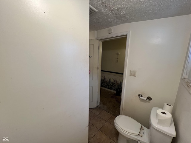 bathroom with toilet, tile patterned flooring, visible vents, and a textured ceiling