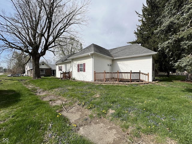 view of side of home with roof with shingles, a yard, and a wooden deck