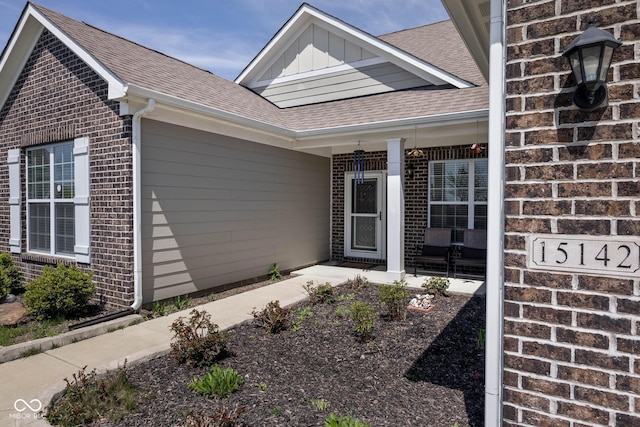 entrance to property with board and batten siding, a shingled roof, brick siding, and covered porch