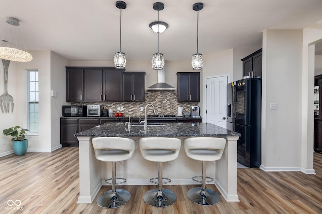 kitchen with dark stone counters, tasteful backsplash, black appliances, light wood-type flooring, and a kitchen bar
