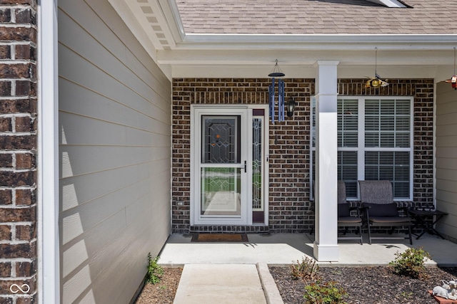 property entrance featuring a shingled roof, covered porch, and brick siding